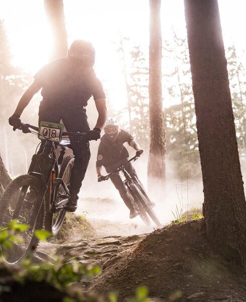 Zwei Mountainbiker fahren hintereinander auf einem Pfad durch den Wald, unter ihnen neblige Luft über dem Boden.