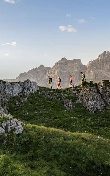 Eine Wandergruppe steht auf einem felsigen Hügelrücken mit eindrucksvoller Dolomitenkulisse im Hintergrund. | © Harald Wisthaler